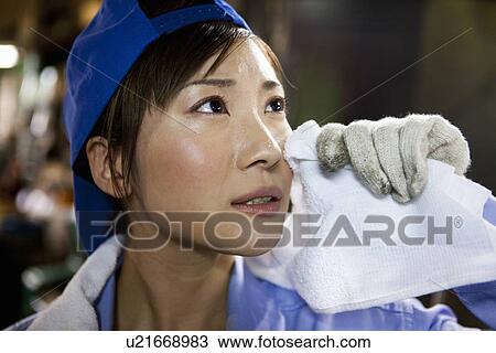 Stock Image - Young Female Factory Worker Wiping Face. Fotosearch
