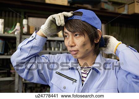 Stock Image - Young Male Factory Worker Putting on Cap. Fotosearch