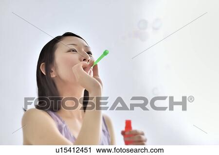 Stock Image - Young woman blowing bubbles. Fotosearch
