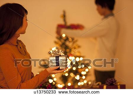 Young Woman Holding Christmas Present, Boyfriend In Background View Large Photo Image Stock Image - Young Woman Holding Christmas Present, Boyfriend In Background. Fotosearch