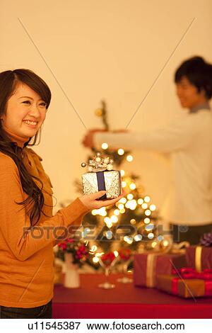 Young Woman Holding Christmas Present, Boyfriend In Background View Large Photo Image Stock Photo - Young Woman Holding Christmas Present, Boyfriend In Background. Fotosearch