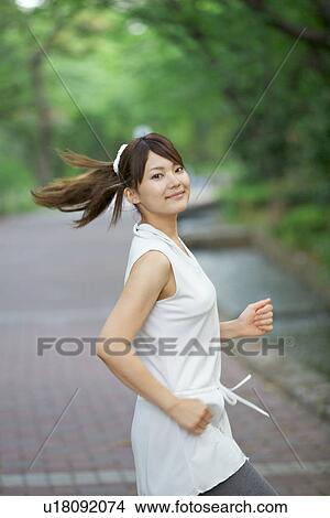 Picture - Young Woman Jogging Along Riverside by Spring Trees. Fotosearch