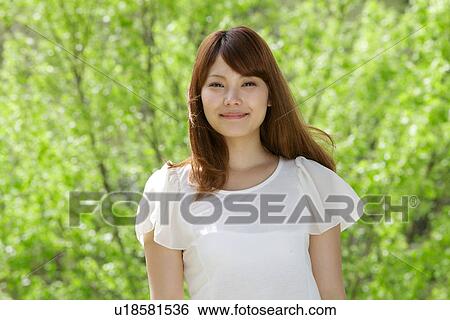 Stock Photograph - Young Woman Smiling In Front Of Budding Forest. Fotosearch