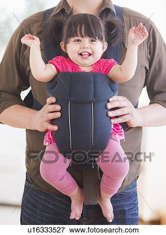 Stock Photo - Baby girl (12-17 months) in baby carrier held by her father. Fotosearch