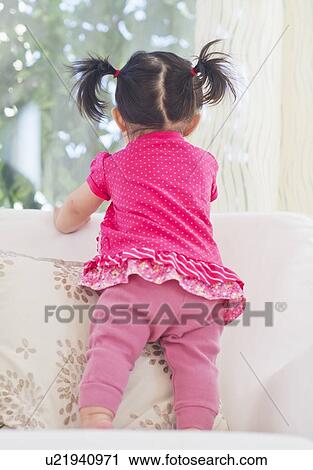Stock Image - Baby girl (12-17 months) looking through window. Fotosearch