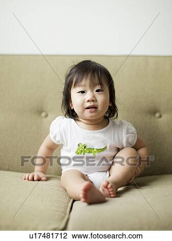 Stock Image - Baby girl (12-17 months) on sofa. Fotosearch