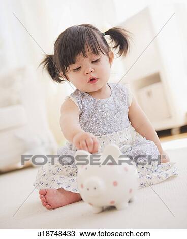 Stock Image - Baby girl (12-17 months) playing with piggy bank. Fotosearch
