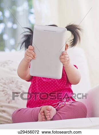Stock Image - Baby girl (12-17 months) playing with digital tablet. Fotosearch