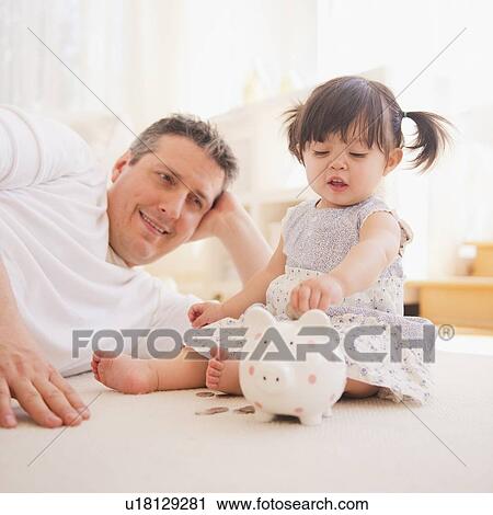 Baby girl (12-17 months) with father playing with piggy bank View Large Photo Image Stock Image - Baby girl (12-17 months) with father playing with piggy bank. Fotosearch