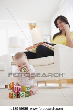 Baby girl (6-11 months) playing with blocks, mother using laptop at home View Large Photo Image Stock Photograph - Baby girl (6-11 months) playing with blocks, mother using laptop at home. Fotosearch