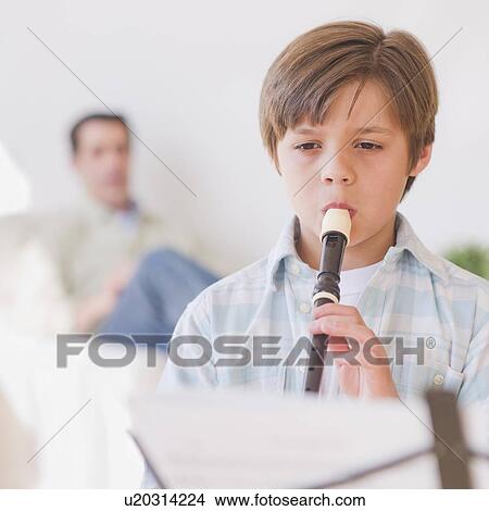 Picture - Boy (10-11 years) playing flute with father in background. Fotosearch
