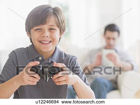 Boy (10-11 years) playing video game with father sitting in background View Large Photo Image Picture - Boy (10-11 years) playing video game with father sitting in background. Fotosearch
