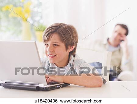 Boy (10-11 years) using laptop at table with father sitting in background View Large Photo Image Stock Photograph - Boy (10-11 years) using laptop at table with father sitting in background. Fotosearch
