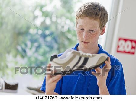 Boy (16-17) looking at shoe in shoe store View Large Photo Image Stock Photo - Boy (16-17) looking at shoe in shoe store. Fotosearch