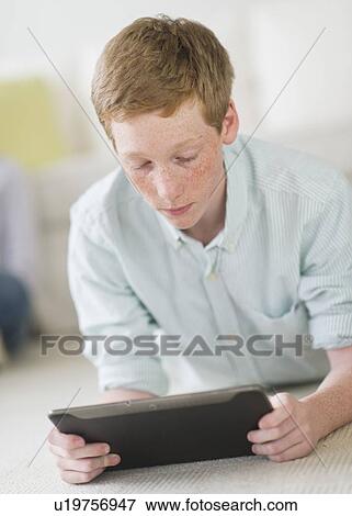 Boy (16-17) lying on floor using tablet pc View Large Photo Image Stock Photo - Boy (16-17) lying on floor using tablet pc. Fotosearch