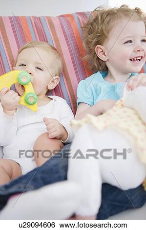 Stock Photograph - Brother and sister (2-3, 6-11 months) sitting on sofa. Fotosearch