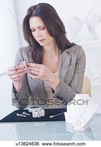 Businesswoman checking quality of jewelry at desk View Large Photo Image Stock Photograph - Businesswoman checking quality of jewelry at desk. Fotosearch