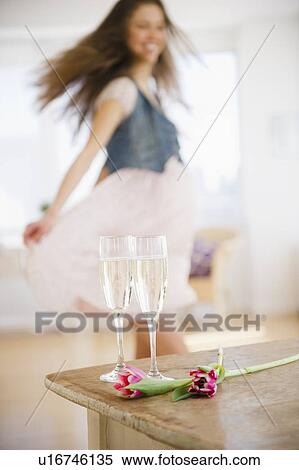 Stock Photography - Champagne flutes on table, woman dancing in background. Fotosearch