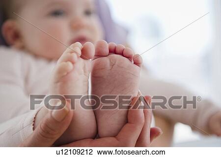 Stock Image - Close up of mother's hand holding baby daughter's (6-11 months) feet. Fotosearch
