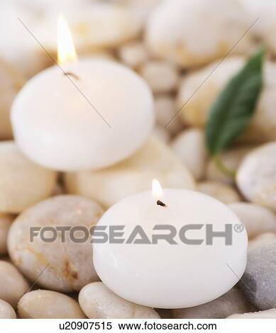 Stock Photography - Close up of tea lights and green leaf on pebble stones, studio shot. Fotosearch