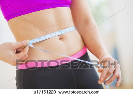Stock Image - Close up of woman measuring herself with tape measure. Fotosearch