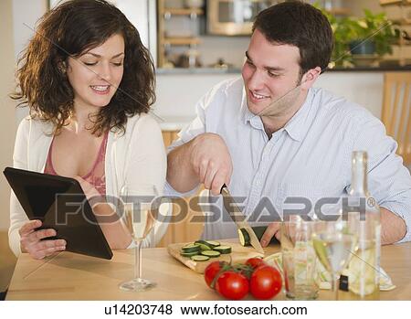 Couple preparing meal and using digital tablet View Large Photo Image Stock Photo - Couple preparing meal and using digital tablet. Fotosearch