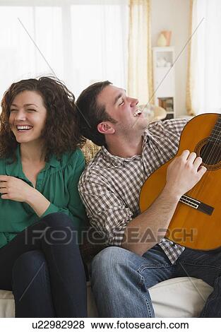Stock Photo - Couple sitting on sofa, man playing guitar. Fotosearch