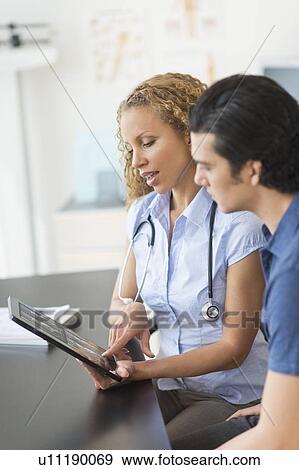 Stock Photo - Doctor and patient talking in clinic using tablet pc. Fotosearch