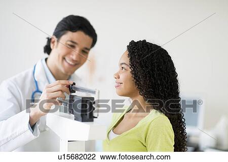 Stock Image - Doctor weighing female patient (10-11). Fotosearch