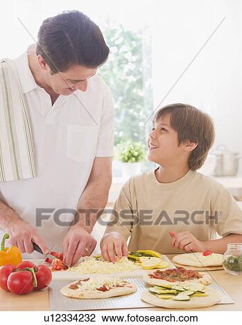 Stock Image - Father and son (10-11 years) preparing pizza. Fotosearch