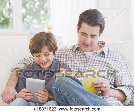 Father and son (10-11 years) sitting on sofa with book and digital tablet View Large Photo Image Stock Image - Father and son (10-11 years) sitting on sofa with book and digital tablet. Fotosearch