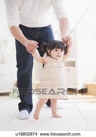 Father helping baby daughter (12-17 months) with her firsts steps View Large Photo Image Picture - Father helping baby daughter (12-17 months) with her firsts steps. Fotosearch
