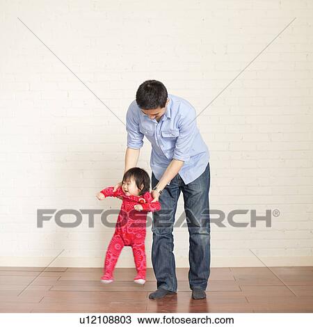 Stock Image - Father helping baby girl (12-17 months) with her first steps. Fotosearch