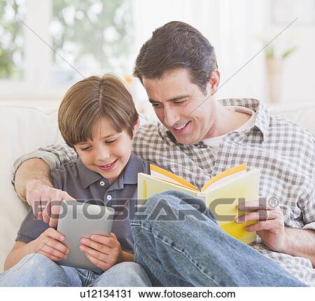 Stock Image - Father teaching son (10-11 years) how to use digital tablet. Fotosearch