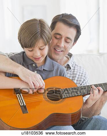Stock Photograph - Father teaching son (10-11 years) how to play acoustic guitar. Fotosearch
