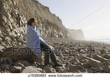 France, Pas-de-Calais, Escalles, Woman wrapped in blanket sitting on rocky beach View Large Photo Image Stock Image - France, Pas-de-Calais, Escalles, Woman wrapped in blanket sitting on rocky beach. Fotosearch