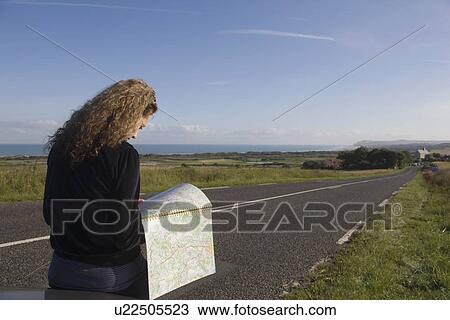 Stock Image - France, Pas-de-Calais, Escalles, Young woman reading map on roadside. Fotosearch