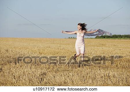 Stock Image - France, Picardie, Albert, Young woman running through stubble with shawl. Fotosearch