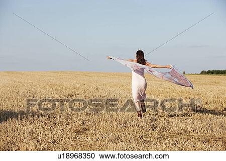 Stock Image - France, Picardie, Albert, Young woman running through stubble with shawl. Fotosearch