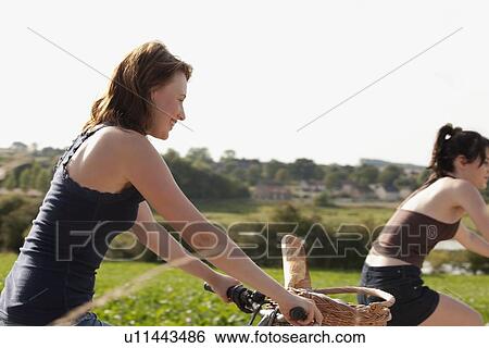Stock Photograph - France, Picardie, Albert, Young women on bikes on country road. Fotosearch