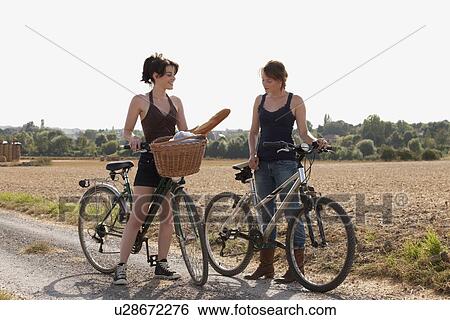 Stock Photograph - France, Picardie, Albert, Young women on bikes on country road. Fotosearch