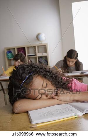 Stock Photograph - Girl (10-11) napping on desk with girl (12-13) and boy (10-11) in background. Fotosearch