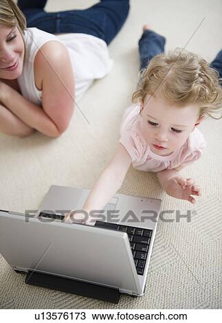Stock Image - Girl (2-3) using laptop, mother in background. Fotosearch
