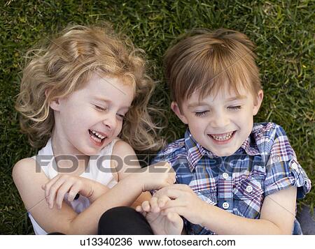 Stock Photograph - Girl (4-5) and boy (6-7) playing on grass. Fotosearch