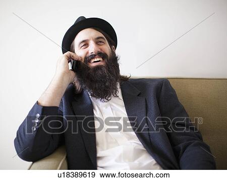 Happy bearded young man sitting on sofa View Large Photo Image Stock Photo - Happy bearded young man sitting on sofa. Fotosearch