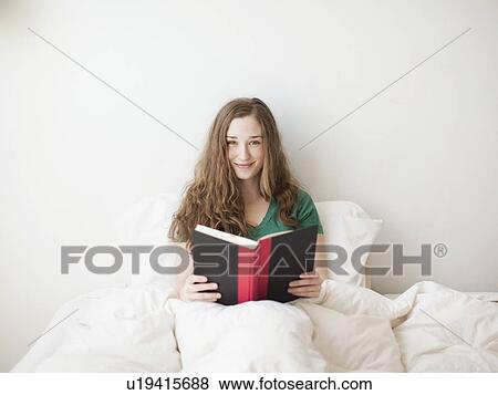 Stock Photo - Happy young attractive woman sitting in bed with book. Fotosearch