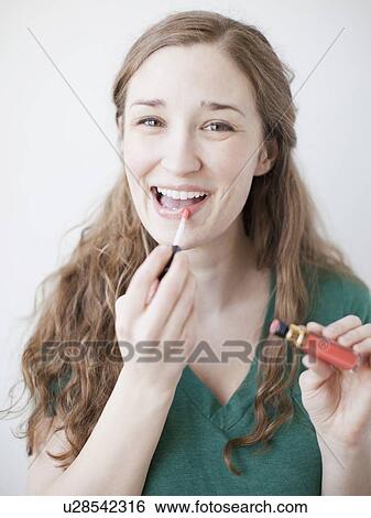 Stock Photograph - Happy young woman applying lipstick. Fotosearch