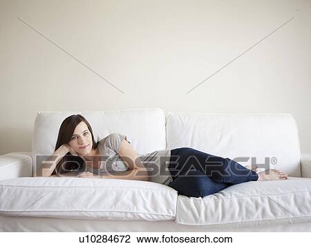 Stock Image - Happy young woman reclining on bed. Fotosearch
