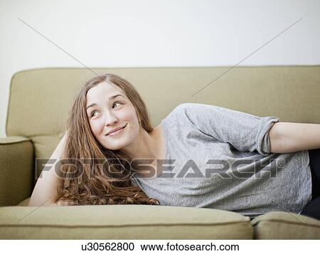 Stock Image - Happy young woman reclining on sofa. Fotosearch