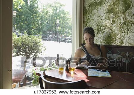 Stock Image - Holland, Amsterdam, Woman sitting with book in cafe window. Fotosearch